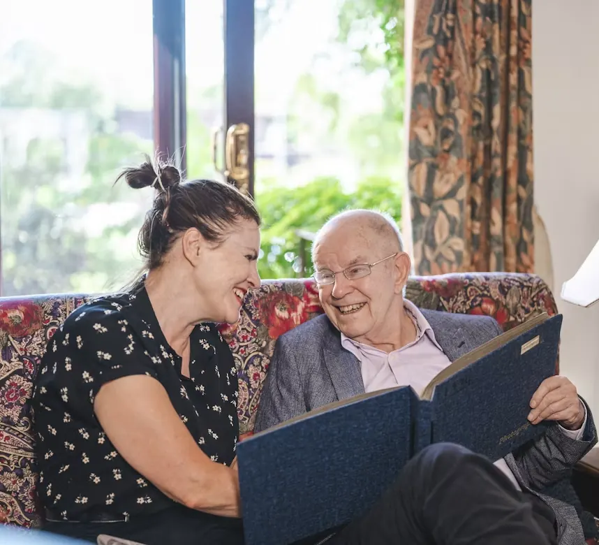 An older man and a woman laughing together as they look through a folder of papers