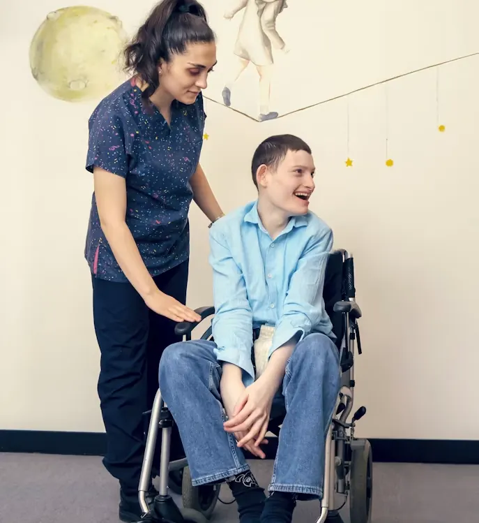 A smiling young man in a wheelchair with his support worker beside him